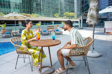 تقوية الروابط الزوجية, الاستجمام والترويح عن النفس في الهواء الطلق، اجواء عائلية سعيدة, مفهوم التحدث ومناقشة الاخبار, زوجان عربيان خليجيان إماراتيان يرتديان الزي الكاجوال يجلسان في إحدى المنتجعات في الإمارات و يتناولان المشروبات المنعشة الطازجة