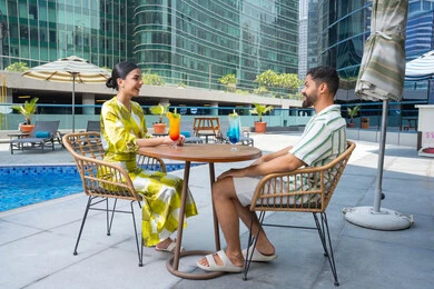 الاستجمام والترويح عن النفس في الهواء الطلق،  اجواء عائلية سعيدة, مفهوم التحدث ومناقشة الاخبار, زوجان عربيان خليجيان إماراتيان يرتديان الزي الكاجوال يجلسان في إحدى المنتجعات في الإمارات و يتناولان المشروبات المنعشة الطازجة