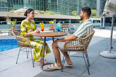 شرب العصائر المنعشة, الإستجمام في الهواء الطلق, قضاء الأوقات المسلية, القيام بالأنشطة الممتعة في الإجازة, زوجان عربيان خليجيان إماراتيان يرتديان الزي الكاجوال يجلسان في إحدى المنتجعات في الإمارات