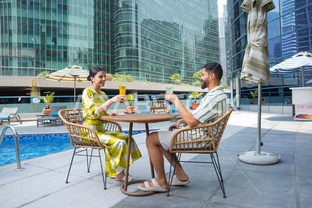 The concept of affection and intimacy, drinking refreshing juices, relaxing outdoors, spending enjoyable time, doing fun activities on vacation, an Emirati Gulf Arab couple wearing casual clothes sitting in one of the resorts in the Emirates