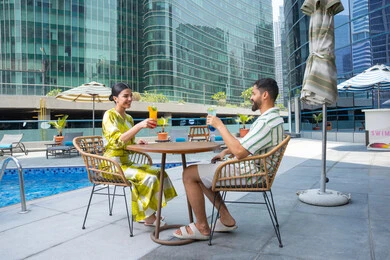 مفهوم المودة والالفة, شرب العصائر المنعشة, الإستجمام في الهواء الطلق, قضاء الأوقات المسلية, القيام بالأنشطة الممتعة في الإجازة, زوجان عربيان خليجيان إماراتيان يرتديان الزي الكاجوال يجلسان في إحدى المنتجعات في الإمارات