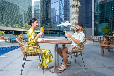 الالفة والمحبة بين الزوجين، اجواء عائلية سعيدة, مفهوم التحدث ومناقشة الاخبار, زوجان عربيان خليجيان إماراتيان يرتديان الزي الكاجوال يجلسان في إحدى المنتجعات في الإمارات و يتناولان المشروبات المنعشة الطازجة