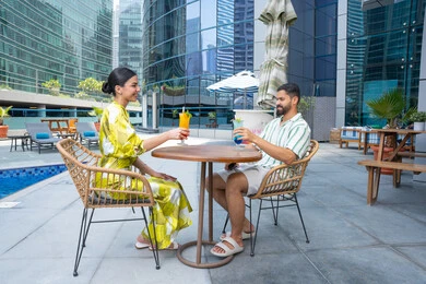 أنشطة عائلية ترفيهيه، محاولة التخفيف من حرارة الصيف بالمشروبات المنعشة، الإستجمام في الهواء الطلق, قضاء الأوقات المسلية, القيام بالأنشطة الممتعة في الإجازة, زوجان عربيان خليجيان إماراتيان يرتديان الزي الكاجوال يجلسان في إحدى المنتجعات في الإمارات