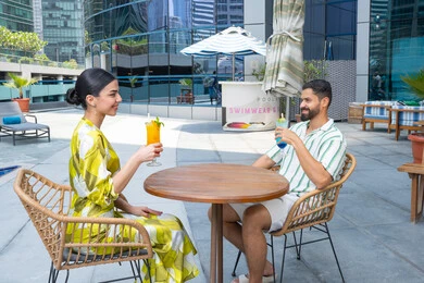 حوارات و نقاشات على المائدة, أنشطة عائلية ترفيهيه، محاولة التخفيف من حرارة الصيف بالمشروبات المنعشة، الإستجمام في الهواء الطلق, قضاء الأوقات المسلية, القيام بالأنشطة الممتعة في الإجازة, زوجان عربيان خليجيان إماراتيان يرتديان الزي الكاجوال يجلسان في إحدى المنتجعات في الإمارات