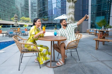 Summer vacation tourism and taking souvenir photo, taking memorable selfies, outdoor recreation, spending fun family time, engaging in enjoyable recreational activities, an Emirati Gulf Arab couple wearing casual clothes sitting in a resort in the Emirates and enjoying cold drinks