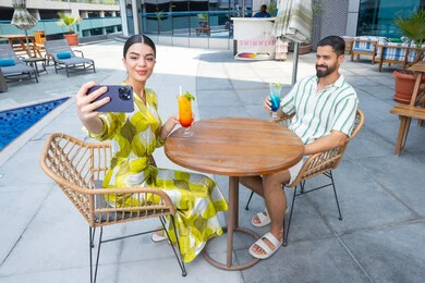 مفهوم السياحة والسفر والقيام بالجولات, التقاط صور السيلفي، الإستجمام في الهواء الطلق, قضاء الأوقات العائلية المسلية, القيام بالأنشطة الترفيهية الممتعة, زوجان عربيان خليجيان إماراتيان يرتديان الزي الكاجوال يجلسان في إحدى المنتجعات في الإمارات و يتناولان المشروبات الباردة