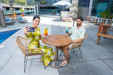 توثيق اللحظات العائلية السعيدة، التقاط صور السيلفي التذكارية، الإستجمام في الهواء الطلق, قضاء الأوقات العائلية المسلية, القيام بالأنشطة الترفيهية الممتعة في الإجازة, زوجان عربيان خليجيان إماراتيان يرتديان الزي الكاجوال يجلسان في إحدى المنتجعات في الإمارات و يتناولان المشروبات الباردة