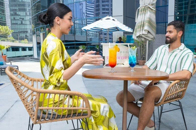 Refreshing seasonal fruit drinks, conversation, outdoor recreation, fun family time, enjoyable leisure activities during vacation, an Emirati Gulf Arab couple in casual attire sitting in a resort in the UAE
