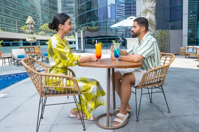 الاستمتاع بالمشروبات الباردة المنعشة, الإستجمام في الهواء الطلق, قضاء الأوقات العائلية المسلية, القيام بالأنشطة الترفيهية الممتعة في الإجازة, زوجان عربيان خليجيان إماراتيان يرتديان الزي الكاجوال يجلسان في إحدى المنتجعات في الإمارات