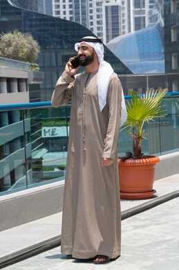 اتصالات ومكالمات هاتفية عبر الهاتف المحمول, تبادل الأخبار مع الأهل والأصدقاء، الدردشة باستخدام الموبايل، الإستجمام في الهواء الطلق, المشي على حدود البركة المائية, رجل عربي خليجي اماراتي يرتدي الكندورة والغترة و يقوم بالتنزه حول الممشى
