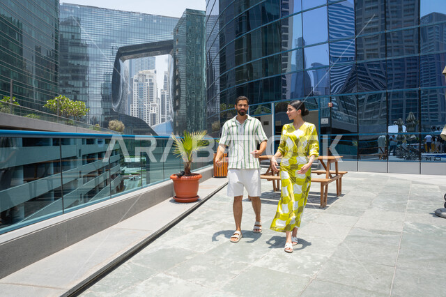 Walking along the edge of the swimming pool, an Emirati couple dressed casually enjoying a stroll; a happy family atmosphere; water sports activities; enjoying summer vacations; pleasant times at a tourist resort.