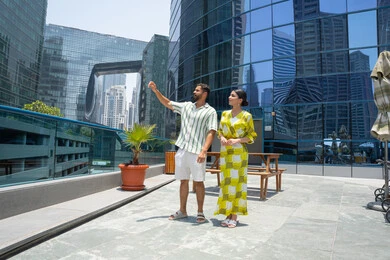 جودة الحياة في الاجازة، تغيير الاجواء المنزلية, الاشارة باصبع السبابة الى شئ ما, انشطة ترفيهية مائية, الاستمتاع بالرحلات الصيفية, قضاء الاوقات ممتعة، المشي على حدود بركة السباحة، زوجان عربيان خليجيان اماراتيان يرتديان الزي الكاجوال و يقومان بالتنزه