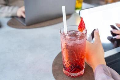 A close-up image of a refreshing drink, integrating modern technologies into daily life, spending enjoyable times with friends, building and enhancing relationships and friendships, a business meeting in a location outside the company headquarters, two Arab Gulf Emirati colleagues sitting at a table in a high-end restaurant in the UAE using a laptop.