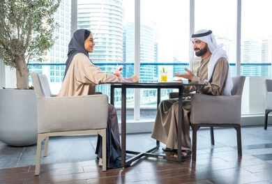 قضاء اوقات ممتعة مع الأصدقاء، إيماءات السعادة والسرور،بناء وتعزيز العلاقات والصداقات، مناقشة الاعمال وتبادل الافكار، اجتماع عمل في مكان خارج مقر الشركة, زميلان عمل عربيان خليجيان إماراتيان يجلسان على طاولة في أحد المطاعم الراقية في الإمارات، يتبادلان الاحاديث والابتسامات