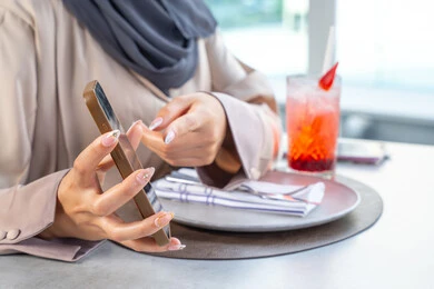 استخدام الهاتف المحمول ، قضاء اوقات ممتعة مع الأصدقاء، بناء وتعزيز العلاقات والصداقات، مناقشة الاعمال وتبادل الافكار، اجتماع عمل في مكان خارج مقر الشركة, امراه عربيه خليجيه اماراتيه ترتدي العباءه والحجاب تجلس على طاولة في أحد المطاعم الراقية في الإمارات تقوم بعرض شاشه الجوال