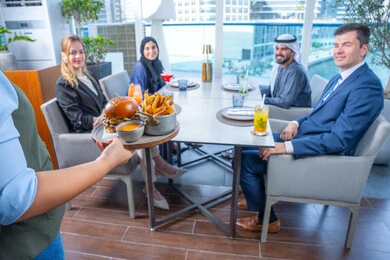 A waiter is taking orders, seafood and healthy dishes, sharing enjoyable moments, enjoying cold drinks, a business meeting in a place outside the company headquarters, building successful social relationships, a group of foreign and Arab friends, Gulf Emiratis sitting at a table in one of the restaurants in the UAE.