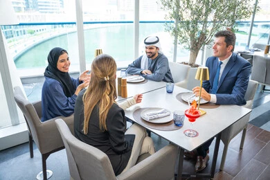 الاستمتاع بتناول المشروبات الباردة، مشاركة الأوقات الممتعة, اجتماع عمل في مكان خارج مقر الشركة, بناء علاقات اجتماعية ناجحة, مجموعة من الأصدقاء الاجانب والعرب خليجيين إماراتيين يجلسون على طاولة في إحدى المطاعم في الإمارات
