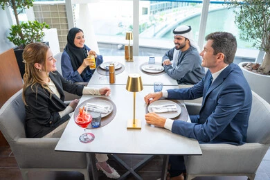 مشاركة الأوقات الممتعة, الاستمتاع بتناول المشروبات الباردة، اجتماع عمل في مكان خارج مقر الشركة, بناء علاقات اجتماعية ناجحة, مجموعة من الأصدقاء الاجانب والعرب خليجيين إماراتيين يجلسون على طاولة في إحدى المطاعم في الإمارات