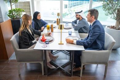 Gestures of joy and happiness, sharing enjoyable moments, enjoying cold drinks, a business meeting in a place outside the company headquarters, building successful social relationships, a group of foreign and Arab friends, Gulf Emiratis sitting at a table in one of the restaurants in the UAE.