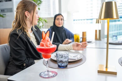 Building successful social relationships, a group of foreign and Arab friends, Emirati Gulf nationals, sitting at a table in a restaurant in the UAE, sharing enjoyable moments, enjoying cold drinks, a business meeting in a location outside the company headquarters.