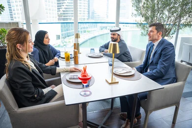 Enjoying cold drinks, sharing fun times, a business meeting in a place outside the company headquarters, building successful social relationships, a group of foreign and Arab friends, Gulf Emiratis sitting at a table in one of the restaurants in the UAE.