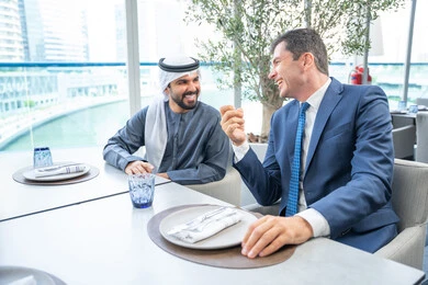 مجموعة من الأصدقاء الاجانب والعرب خليجيين إماراتيين يجلسون على طاولة في إحدى المطاعم في الإمارات، مشاركة الأوقات الممتعة, الاستمتاع بتناول المشروبات الباردة، اجتماع عمل في مكان خارج مقر الشركة, بناء علاقات اجتماعية ناجحة