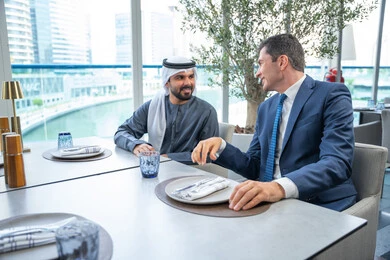 بناء علاقات اجتماعية ناجحة, مجموعة من الأصدقاء الاجانب والعرب خليجيين إماراتيين يجلسون على طاولة في إحدى المطاعم في الإمارات، مشاركة الأوقات الممتعة, الاستمتاع بتناول المشروبات الباردة، اجتماع عمل في مكان خارج مقر الشركة