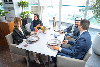 A business meeting in a place outside the company headquarters, sharing enjoyable moments, enjoying cold drinks, building successful social relationships, a group of foreign and Arab friends, Gulf Emiratis sitting at a table in one of the restaurants in the UAE.
