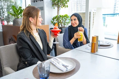 الاستمتاع بتناول المشروبات الباردة، مشاركة الأوقات الممتعة, اجتماع عمل في مكان خارج مقر الشركة, بناء علاقات اجتماعية ناجحة, مجموعة من الأصدقاء الاجانب والعرب خليجيين إماراتيين يجلسون على طاولة في إحدى المطاعم في الإمارات