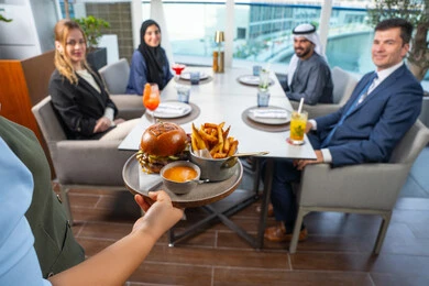 Service in one of the Emirati restaurants, a waiter serving Western dishes, a business meeting in a place outside the company headquarters, spending enjoyable times with friends, a fun and social gathering, a group of Arab Gulf Emirati friends sitting at the table in one of the restaurants in the UAE, enjoying their favorite meals.
