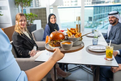 مجموعة من الأصدقاء العرب الخليجين الاماراتيين يجلسون على المائدة في إحدى المطاعم في الإمارات، خدمة في احدى المطاعم الأماراتية، نادل يقدم الأطباق الغربية، اجتماع عمل في مكان خارج مقر الشركة,قضاء أوقات ممتعة مع الأصدقاء، جلسة وناسة وتعارف، تناول الوجبات المفضلة