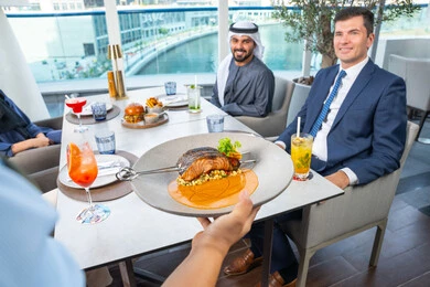 Spending enjoyable times with friends, a fun and social gathering, service in one of the Emirati restaurants, a waiter serving Western dishes, a business meeting in a place outside the company headquarters, a group of Arab Gulf Emirati friends sitting at the table in one of the restaurants in the UAE, enjoying their favorite meals.