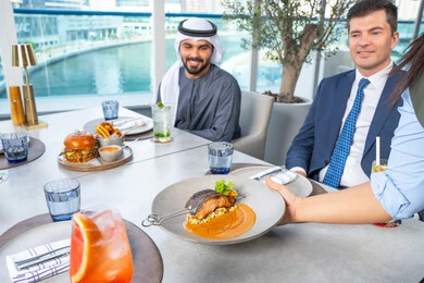 مجموعة من الأصدقاء العرب الخليجين الاماراتيين يجلسون على المائدة في إحدى المطاعم في الإمارات، خدمة في احدى المطاعم الأماراتية، نادل يقدم الأطباق الغربية، اجتماع عمل في مكان خارج مقر الشركة,قضاء أوقات ممتعة مع الأصدقاء، جلسة وناسة وتعارف، تناول الوجبات المفضلة