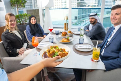 A business meeting in a place outside the company headquarters, spending enjoyable times with friends, service in one of the Emirati restaurants, a waiter serving Western dishes, a fun and social gathering, a group of Arab Gulf Emirati friends sitting at the table in one of the restaurants in the UAE, enjoying their favorite meals.