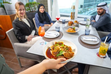 مجموعة من الأصدقاء العرب الخليجين الاماراتيين يجلسون على المائدة في إحدى المطاعم في الإمارات، خدمة في احدى المطاعم الأماراتية، نادل يقدم الأطباق الغربية، اجتماع عمل في مكان خارج مقر الشركة,قضاء أوقات ممتعة مع الأصدقاء، جلسة وناسة وتعارف، تناول الوجبات المفضلة