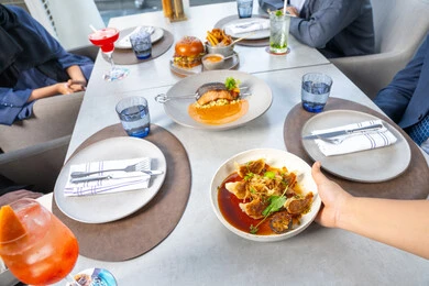 تناول الوجبات المفضلة، خدمة في احدى المطاعم الأماراتية، نادل يقدم الأطباق الغربية، اجتماع عمل في مكان خارج مقر الشركة,قضاء أوقات ممتعة مع الأصدقاء، جلسة وناسة وتعارف، مجموعة من الأصدقاء العرب الخليجين الاماراتيين يجلسون على المائدة في إحدى المطاعم في الإمارات