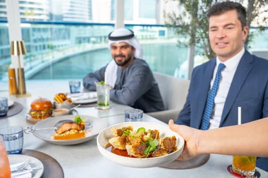 خدمة في احدى المطاعم الأماراتية، نادل يقدم الأطباق الغربية، اجتماع عمل في مكان خارج مقر الشركة,قضاء أوقات ممتعة مع الأصدقاء، جلسة وناسة وتعارف، مجموعة من الأصدقاء العرب الخليجين الاماراتيين يجلسون على المائدة في إحدى المطاعم في الإمارات، تناول الوجبات المفضلة