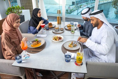 Spending enjoyable times with friends, a table filled with various dishes and drinks, a business meeting in a place outside the company headquarters, sharing fun moments, a group of Arab Gulf Emirati friends sitting at a table in one of the restaurants in the UAE.