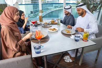 A table filled with various types of food and drinks, spending enjoyable times with friends, a business meeting in a place outside the company headquarters, sharing fun moments, a group of Arab Gulf Emirati friends sitting at a table in one of the restaurants in the UAE.