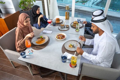 Spending enjoyable times with friends, a table filled with various dishes and drinks, a business meeting in a place outside the company headquarters, sharing fun moments, a group of Arab Gulf Emirati friends sitting at a table in one of the restaurants in the UAE.