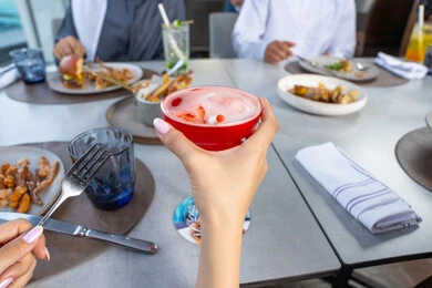 A close-up image of a woman's hand enjoying cold drinks, a business meeting in a location outside the company headquarters, building successful social relationships, a group of Arab friends from the Gulf, Emiratis sitting at a table in one of the restaurants in the UAE, sharing enjoyable moments.