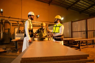 تسجيل الملاحظات والبيانات، جودة الانتاج المحلي الوطني، كتابة و تدوين الملاحظات، مناقشة الخبرات والآراء، صناعة الأثاث المنزلي والمكتبي، ورشات عمل في المملكة العربية السعودية، رجل مهندس عربي خليجي سعودي يرتدي الثوب و خوذة و سترة الحماية يقف برفقة زميلة يقومان بمتابعة سير العمل