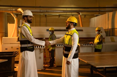 مهن وحرف شعبية تقليدية قديمة، المصافحة والسلام والتوافق على المهام، ورشات عمل في المملكة العربية السعودية, جودة الانتاج المحلي الوطني, صناعة الأثاث المنزلي والمكتبي، رجل مهندس عربي خليجي سعودي يرتدي الثوب الابيض و ستره الحماية يقوم بمصافحة زميله