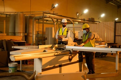 كتابة و تدوين الملاحظات، العمل في القطاع الصناعي، معمل تصنيع الأثاث المنزلي، عامل يقوم بالعمل على جهاز قص الخشب بالليزر، التطور والتقدم التقني في صناعة الخشب، مهندس عربي خليجي سعودي يرتدي الخوذة و ستره الحماية يقوم بالاشراف على العمال