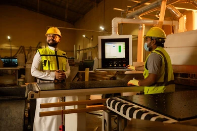 Factories and workshops in the Kingdom of Saudi Arabia, supervising the progress of the work plan, looking at something, workshops and traditional crafts, a Saudi Gulf Arab engineer wearing a thobe, helmet, and safety vest standing inside the factory, wood manufacturing workshop.