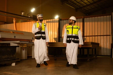 Monitoring the daily performance of laboratory machines, wooden furniture manufacturing workshop, the concept of discussions and dialogues, two Arab Gulf engineers from Saudi Arabia wearing safety vests and helmets supervising the progress of the work plan, popular crafts and manual professions.