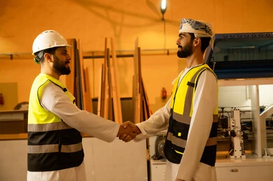 Traditional old popular professions and crafts, manufacturing of home and office furniture, a friendly greeting between colleagues, workshops in the Sultanate of Oman, quality of national local production, an Arab Gulf Omani engineer wearing traditional attire and work uniform shakes hands with his colleague. Traditional old popular professions and crafts, manufacturing of home and office furniture, a friendly greeting between colleagues, workshops in the Sultanate of Oman, quality of national local production, an Arab Gulf Omani engineer wearing traditional attire and work uniform shakes hands with his colleague.