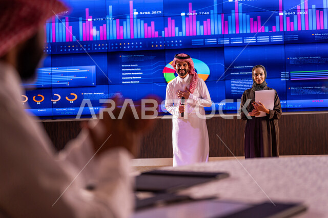 رجل عربي خليجي سعودي يصفق لاداء سيدة ورجل عربيان خليجيان سعوديان في مؤتمر اقتصادي،  شرح سوق الاوراق المالية ،تحليل البيانات المالية ،  الاستثمار المالي والاقتصادي