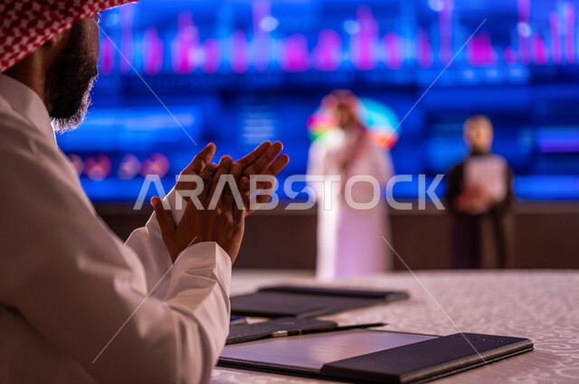 رجل عربي خليجي سعودي يصفق لاداء سيدة ورجل عربيان خليجيان سعوديان في مؤتمر اقتصادي،  شرح سوق الاوراق المالية ،تحليل البيانات المالية ،  الاستثمار المالي والاقتصادي