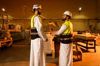 Recording and documenting information, wooden furniture manufacturing workshop, the concept of discussions and dialogues, two Arab Gulf engineers from Saudi Arabia wearing safety vests and helmets supervising the progress of the work plan, popular crafts and manual professions, carpentry workshops in the Kingdom of Saudi Arabia.